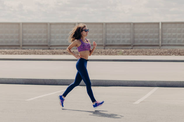 Eine durchtrainierte junge Frau in Sportkleidung, die im Freien auf einer offenen Straße läuft, wobei ihr Haar im Wind weht; sie trägt eine Sonnenbrille und blaue Leggings (Seitenansicht). Eine durchtrainierte junge Frau in Sportkleidung, die im Freien auf einer offenen Straße läuft, wobei ihr Haar im Wind weht; sie trägt eine Sonnenbrille und blaue Leggings (Seitenansicht). (License=RF) 25096371 ,model released, Symbolfoto Copyright: xZoonar.com ViorelxKurnosovx 25096371 ,model released, Symbolfoto ,property released