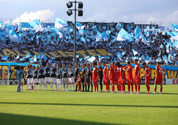 Fussball, Herren, DFB-Pokal, 1.Hauptrunde, Saison 2026 2027, TSV 1860 München - Holstein Kiel, Grünwalder Stadion Einlaufen beider Teams mit der Choreo der 60er Fans in der Westkurve im Hintergrund