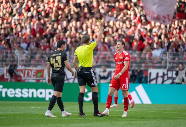 Fußball, Herren, Saison 2026 2027, 1. Bundesliga (5. Spieltag), 1. FC Union Berlin - SV 07 Elversberg, v. l. Felix Keidel (SV Elversberg), Schiedsrichter Tobias Reichel zeigt Tim Skarke (1. FC Union Berlin) die Gelbe Karte, 10.10.2026, Copyright: xMatthiasxKochx