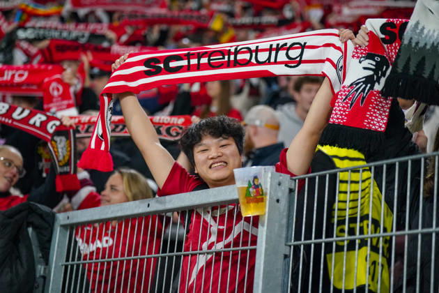 Deutschland: Fussball UEFA Conference League 2026 - 2027, 1. Spieltag - SC Freiburg vs FK Jablonec - Europa-Park-Stadion (Freiburg): Lächelnder Fan des SC Freiburg hält einen rot-weissen Fanschal mit der Aufschrift scfreiburg über den Kopf. Porträt eines begeisterten Anhängers auf der Tribüne des Europa-Park-Stadions beim UEFA Conference League-Spiel gegen FK Jablonec. SC Freiburg, FK Jablonec, Fussball, Europapokal, Fussballfan, Fans, Zuschauer, Fankultur, Fanschal, Vereinsfarben, Vereinswappen, Fanartikel, Merchandising, Emotionen, Begeisterung, Heimfans, Stadion, Tribüne, Supporter, Fanblock. Copyright: xJOERANxSTEINSIEKx