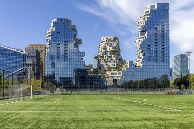Moderne Wohn- und Bürogebäude Valley im Stadtteil Amsterdam Zuid, die Fassaden bestehen aus Glas und spiegeln den blauen Himmel wider, die Bauweise ist außergewöhnlich und besteht aus gestaffelten und versetzten Elementen mit Terrassen, und vor dem Gebäude liegt ein Fußballfeld mit grünem Rasen, Amsterdam, niederländische Hauptstadt, Noord-Holland, Nordholland, Niederlande Modern residential and office buildings Valley in the Amsterdam-Zuid district, the facades are made of glass and reflect the blue sky, the construction is exceptional and consists of staggered and staggered elements with terraces, and a soccer field with green lawn lies in front of the building, Amsterdam, Dutch capital, Noord-Holland, North Holland, Netherlands Copyright: imageBROKER StanislavxBelicka ibxbsb19476152