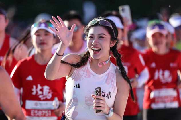 (261018) -- BEIJING, Oct. 18, 2026 -- A runner waves to cameras as she competes during the 2026 Beijing Marathon & National Marathon Championships in Beijing, capital of China, Oct. 18, 2026. ) (SP)CHINA-BEIJING-2026 BEIJING MARATHON(CN) LixMing 