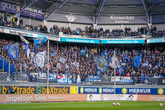 Deutschland: Fussball Bundesliga 2026 - 2027, 7. Spieltag - SC Paderborn vs Hamburger SV - Home-Deluxe-Arena (Paderborn): Fans und Auswärtsfans des Hamburger SV (HSV) auf der Gästetribüne der Home-Deluxe-Arena in Paderborn. Dicht besetzter Gästeblock mit zahlreichen blau-weiss-schwarzen Fahnen, Fanbannern, Transparenten und Schals. Fankultur, Ultras, organisierte Fanszene, Auswärtsspiel, Fussball, Bundesliga, Zuschauer, Stimmung, Support, Fanblock, Tribüne, Totale, Stadion, Sportstätte, Sicherheitszaun, Werbung, Sponsoren, Werbebanden, Merkur, buXtrade, HENKENOTTER. Copyright: xJOERANxSTEINSIEKx