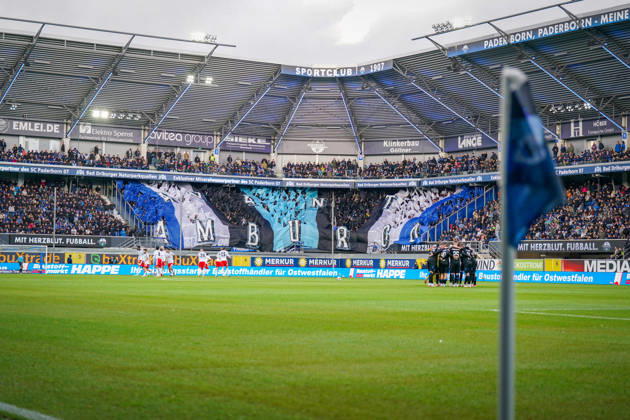 Deutschland: Fussball Bundesliga 2026 - 2027, 7. Spieltag - SC Paderborn vs Hamburger SV - Home-Deluxe-Arena (Paderborn): Totale der Home-Deluxe-Arena in Paderborn, Innenansicht mit grosser blau-schwarz-weisser Choreographie der Heimfans des SC Paderborn 07 auf der Tribüne, Schriftzug HAMBURG. Fanchoreo, Ultras, Fanszene, Zuschauer, Fahnen, Fanblock, Stadion, Sportstätte, Fussball, Bundesliga, Mannschaftskreis, Hamburger SV, SC Paderborn, Eckfahne, Spielfeld, Flutlicht, Stadiondach, Werbung, Sponsoren, Werbebanden, Merkur, buXtrade, Bad Driburger, Happe, Stimmung. Copyright: xJOERANxSTEINSIEKx