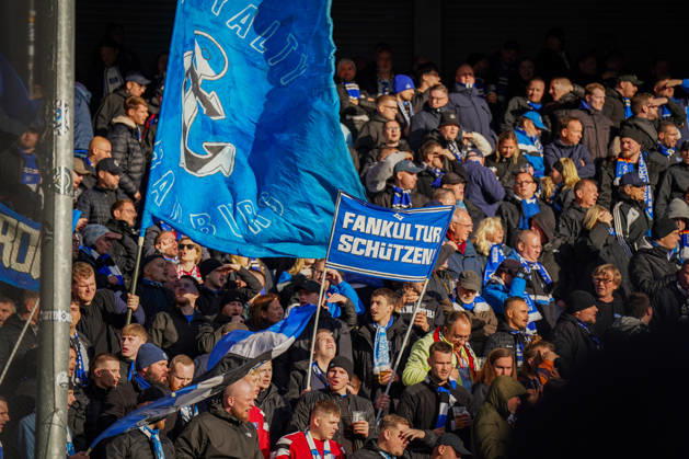 Deutschland: Fussball Bundesliga 2026 - 2027, 7. Spieltag - SC Paderborn vs Hamburger SV - Home-Deluxe-Arena (Paderborn): Auswärtsfans des Hamburger SV (HSV) im Gästeblock der Home-Deluxe-Arena in Paderborn. Grosse blau-schwarze HSV-Fahnen mit Anker und Schriftzug Hamburg, Transparent Fankultur schützen. Fans, Ultras, Fanszene, Fankultur, Fanprotest, Zuschauer, Fahnen, Spruchband, Transparent, Tribüne, Fanblock, Stimmung, Support, Auswärtsspiel, Fussball, Bundesliga, SC Paderborn 07, Hamburger SV, Stadion, Sportstätte, Fanrechte, Fankultur schützen, Totale. Copyright: xJOERANxSTEINSIEKx
