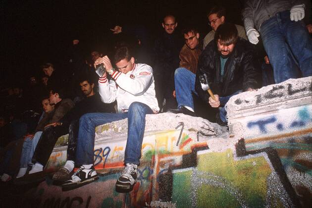 Fall der Berliner Mauer - Junge Männer hämmern auf die Mauer ein