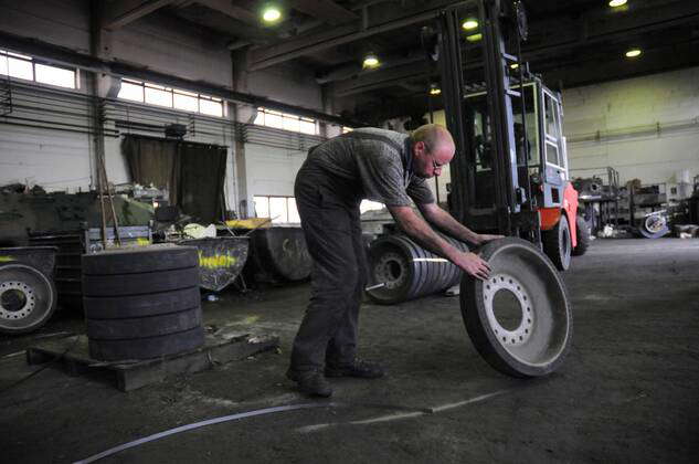 Mitarbeiter mit Bauteilen eines zerlegten Panzers in der Battle Tank Dismantling