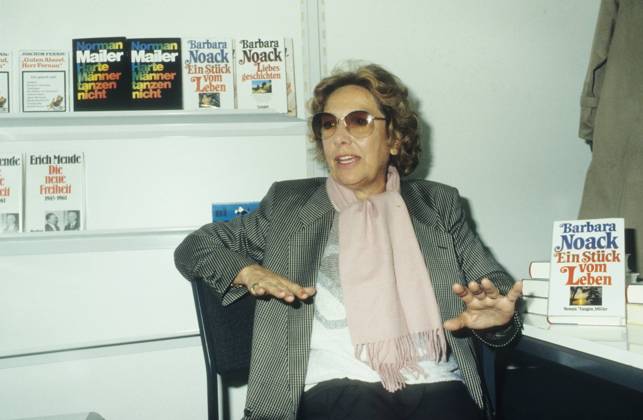 Barbara Noack (Autorin) 10 84 hör Autor Frau Literatur Buch Schriftstellerei Locken weißhaarig leger Blazer Schal Pullover sitzend aufstützend Titel Schild Ein Stück vom Leben Regal Bücherregal Tisch Brille sprechend gestikulierend halb quer