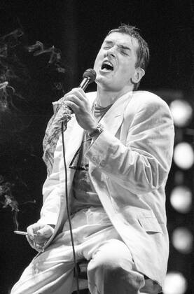 Falco (Sänger, Musiker) 10 86 dar Falco bei einem Konzert im Oktober 1986 Mann Gesang Musik Pop Rock Künstler Österreicher Österreich österreichisch österreichischer Johann Hölzel Bühne Auftritt Show seriös sitzend Hocker Barhocker singend Mikrofon Mikro Hemd Jackett Sakko Zigarette haltend Augen geschlossen dunkelhaarig Gelfrisur zurückgekämmt halb Singer Music Musician Performance Stage hoch sw