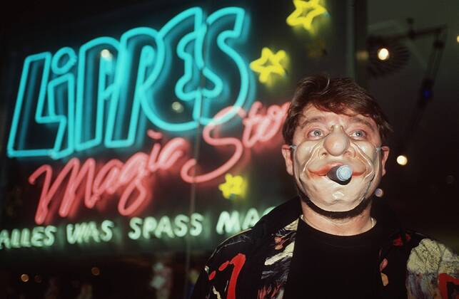 Jürgen von der Lippe vor seinem Laden Lippes Magic Store 05 98 pp Mann TV Fernsehen Schauspiel Moderation Show Komik Kabarett Comedy Musik Gesang dunkelhaarig leger T-Shirt Hemd Bart stehend Schild Logo Geschäft halb quer Maske tragend