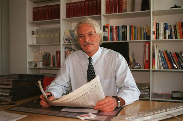 Thomas Roth (TV-Journalist) 07 02 te Mann Journalismus TV Fernsehen Korrespondent Korrespondenz weißhaarig kurzhaarig Schnäuzer Brille leger Hemd Krawatte sitzend Büro Tisch Schreibtisch halb quer nachdenklich lächelnd aufschauend Stift haltend Unterlagen Zeitung aufgeschlagen hinter ihm Regal Bücher Bücherregal Fototermin Thomas Roth am 30.07.2002 in Berlin