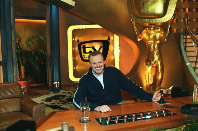 Stefan Raab in tv total (ProSieben) 01 03 pp Mann Moderator TV Fernsehen Moderation Musiker Musik Pop Gesang Sänger Produktion Unterhaltung Show dunkelhaarig kurzhaarig leger Trainingsjacke Sportjacke Shirt sitzend TV-Studio Kulisse Dekoration Logo halb quer sitzend lächelnd Tisch Moderationstisch Pult Glas Wasserglas Fototermin tv total (ProSieben) am 06.01.2003 in Köln