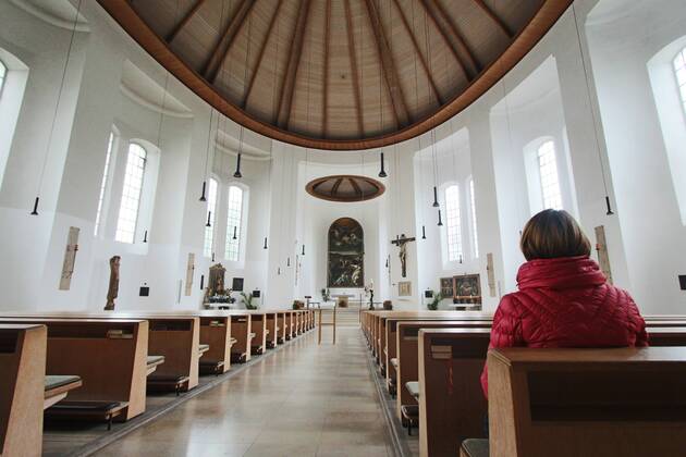 Frau sitzt allein auf der Kirchenbank in einer katholischen Kirche in München und hält Andacht (model released)