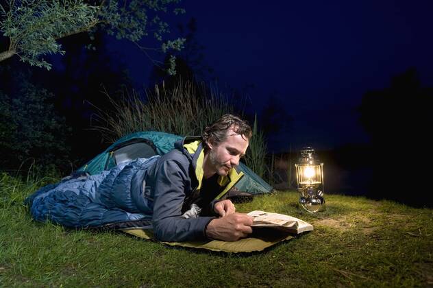Germany, Bavaria, Ammersee, Man reading book near lakeshore while camping at night model released  RNF000615