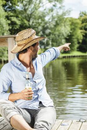 Man sitting on platform at the waterside with beer bottle pointing his finger model released Symbolfoto property released  FMKF001966
