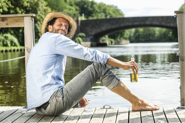 Smiling man sitting on platform at the waterside with beer bottle model released Symbolfoto property released  FMKF001983