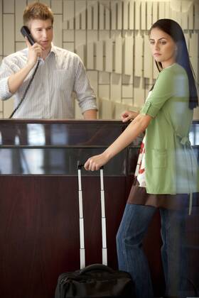 Woman standing at hotel reception with rolling suitcase model released Symbolfoto property released TOYF001348