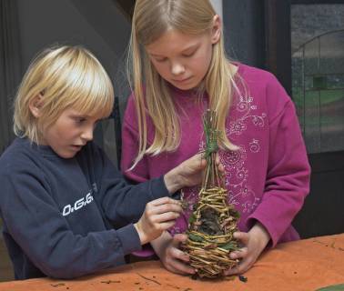 zwei Kinder flechten aus Weidenzweigen eine Nistkugel fuer Voegel, Nest wird mit Moos und Schilfblueten ausgekleidet, Deutschland nesting material for ball nest, two children braiding willow branches and coating with moss and reeds, Germany BLWS416031 Copyright: xblickwinkel F.xHeckerx