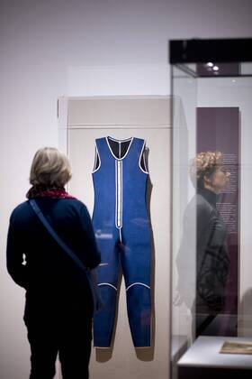 The British View Germany - Memories of a Nation, Exhibition Gropius-Bau DEU, Deutschland, Germany, Berlin, 07.10.2016 Besucher neben dem Surfanzug von 1987, Symbol fuer die Flucht ueber Wasser aus der DDR, in der Ausstellung Der Britische Blick Deutschland - Erinnerungen einer Nation, The British View German - Memories of a Nation, im Martin-Gropius-Bau in Berlin. Die Ausstellung eroeffnet am 08. Oktober und geht bis 09. Januar und praesentiert ca 200 Objekte welche einen Bezug zu den letzten 600 Jahre Geschichte in Deutschland haben. Sie zeigt Spuren deutscher Identitaet aus britischer Perspektive. Visitor next to a Wetsuit from 1987, a symbol for the escape out of the former GDR, on display during his exhibition Der Britische Blick Deutschland - Erinnerungen einer Nation, The British View German - Memories of a Nation, at the Martin Gropius Bau in Berlin, Germany. The exhibition opens