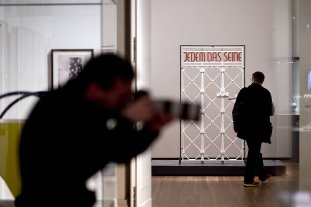 The British View Germany - Memories of a Nation, Exhibition Gropius-Bau DEU, Deutschland, Germany, Berlin, 07.10.2016 Besucher betrachtet das Lagertor des Konzentrationslager KZ Buchenwald mit der Inschrift Jedem das Seine in der Ausstellung Der Britische Blick Deutschland - Erinnerungen einer Nation, The British View German - Memories of a Nation, im Martin-Gropius-Bau in Berlin. Die Ausstellung eroeffnet am 08. Oktober und geht bis 09. Januar und praesentiert ca 200 Objekte welche einen Bezug zu den letzten 600 Jahre Geschichte in Deutschland haben. Sie zeigt Spuren deutscher Identitaet aus britischer Perspektive. Visitor next to a gate from the former Buchenwald concentration camp with the words Jedem das Seine, To Each What He Deserves, on display during his exhibition Der Britische Blick Deutschland - Erinnerungen einer Nation, The British View German - Memories of a Nation, at the