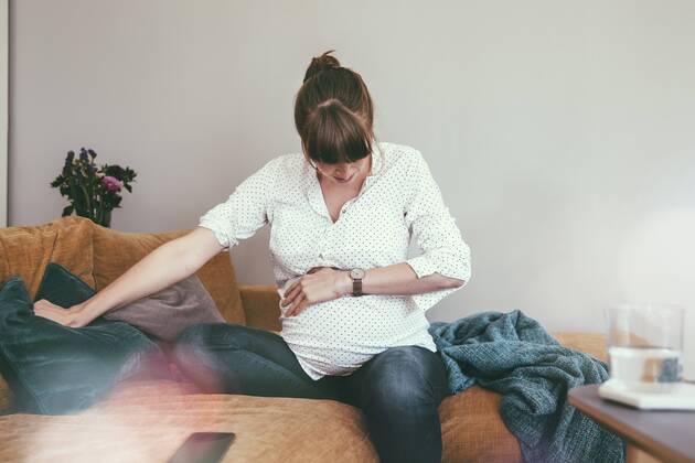 Expectant mother timing her contractions while sitting on couch at home model released Symbolfoto property released MFF03389