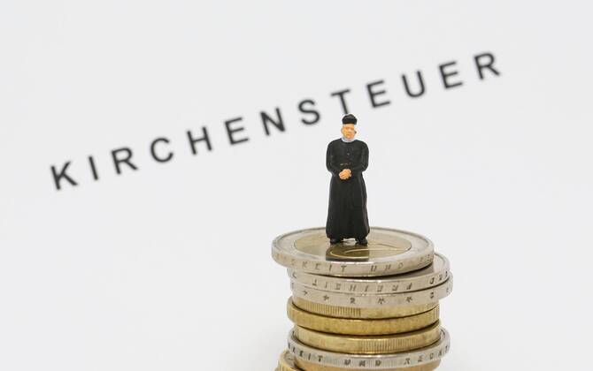 Nuernberg Symbolfoto, Themenbild Kirchensteuer. Geistlicher mit Soutane steht auf Euro Muenzen. Im Hintergrund Schriftzug Kirchensteuer. Copyright: xWuestx Eibner-Pressefotox EP_fwt