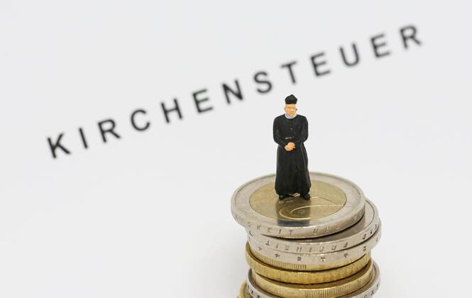 Nuernberg Symbolfoto, Themenbild Kirchensteuer. Geistlicher mit Soutane steht auf Euro Muenzen. Im Hintergrund Schriftzug Kirchensteuer. Copyright: xWuestx Eibner-Pressefotox EP_fwt