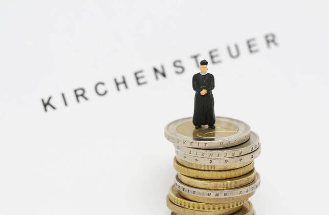 Nuernberg Symbolfoto, Themenbild Kirchensteuer. Geistlicher mit Soutane steht auf Euro Muenzen. Im Hintergrund Schriftzug Kirchensteuer. Copyright: xWuestx Eibner-Pressefotox EP_fwt