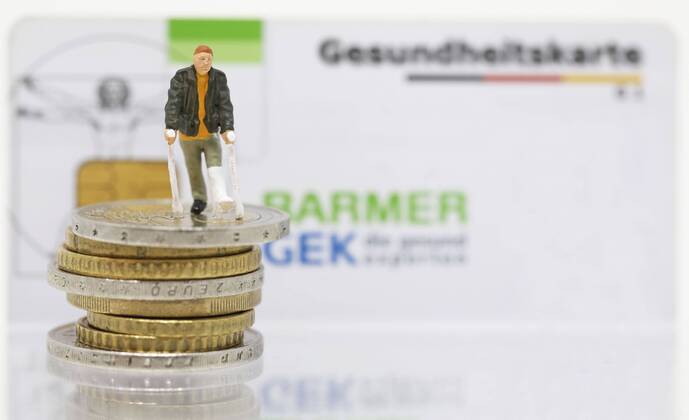 Nuernberg Symbolfoto, Themenbild Krankenversicherung, Krankenkassenbeitrag, Mann mit Gips und Gehhilfe steht auf Euro Muenzen. Im Hintergrund eine Gesundheitskarte der Barmer gek. Copyright: xWuestx Eibner-Pressefotox EP_fwt