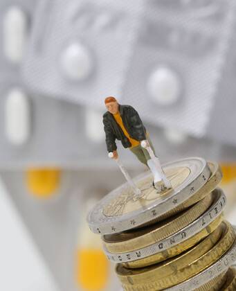 Nuernberg Symbolfoto, Themenbild Krankenversicherung, Krankenkassenbeitrag, Arzneimittelkosten. Mann mit Gips und Gehhilfe steht auf Euro Muenzen. Im Hintergrund verschiedene Arzneimittel. Copyright: xWuestx Eibner-Pressefotox EP_fwt