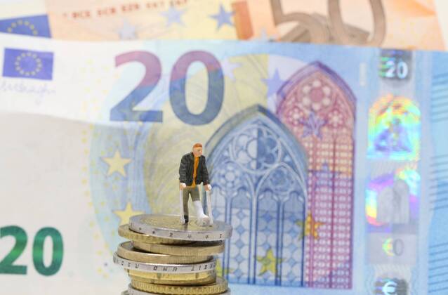 Nuernberg Symbolfoto, Themenbild Krankenversicherung, Krankenkassenbeitrag, Arzneimittelkosten. Mann mit Gips und Gehhilfe steht auf Euro Muenzen. Im Hintergrund verschiedene Euro Banknoten. Copyright: xWuestx Eibner-Pressefotox EP_fwt