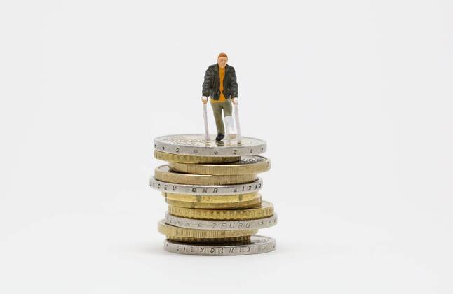 Nuernberg Symbolfoto, Themenbild Krankenversicherung, Krankenkassenbeitrag, Arzneimittelkosten. Mann mit Gips und Gehhilfe steht auf Euro Muenzen. Copyright: xWuestx Eibner-Pressefotox EP_fwt