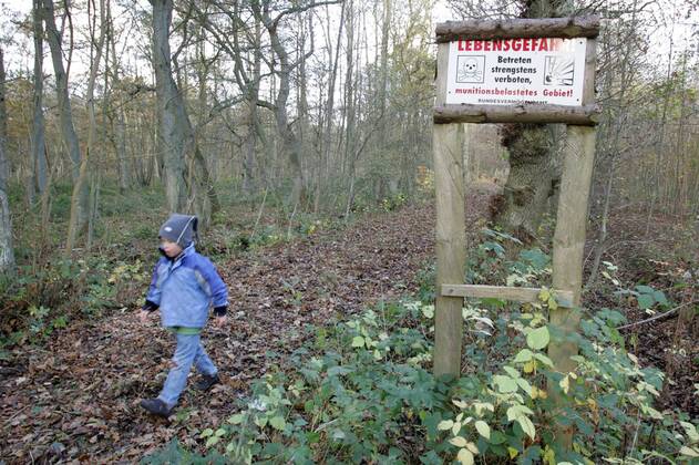 21.11.2005, Zingst, Mecklenburg-Vorpommern, DEU - Ein Kind laeuft auf einem Waldweg mit Hinweisschild Lebensgefahr. (Mensch, Kind, Junge, Maedchen, Kindheit, Bube, Knabe, Gesellschaft, Lebenswelt, Lebenswelten, Freizeit, Urlaub, Reise, Tourismus, Schild, Aufsichtspflicht, gehen, laufen, wandern, Wanderung, Weg, Pfad, Waldweg, verboten, Jahreszeit, Herbst, Laub, Herbstlaub, Warnschild, Warnung, Verbot, Verbotsschild, Hinweis, Lebensgefahr, Gefahr, gefaehrlich, Totenkopf, Staat, Bund, Bundesvermoegensamt, Blindgaenger, Bombe, Bomben, Granaten, Munition, munitionsbelastet, Sprengplatz, Sprengung, sprengen, Hinterlassenschaft, Hinterlassenschaften, Krieg, Kriegsfolgen, Kriegshinterlassenschaft, Kriegshinterlassenschaften, Mine, Minen, Landmine, Landminen, Minenfeld, Minenfelder, Militaer, militaerisch, Aussenaufnahme, Hinweisschild, digital, QF, gefährlich, Bundesvermögensamt, Blindgänger, M MR:N