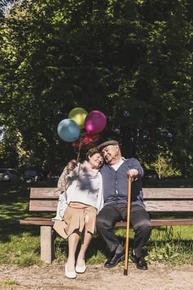 Happy senior couple with balloons sitting on bench in a park model released Symbolfoto  UUF10651