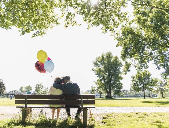 Happy senior couple with balloons sitting on bench in a park model released Symbolfoto  UUF10648