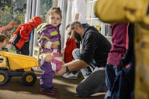 Pre-school teacher helping girl putting on rainwear in kindergarten model released Symbolfoto property released  MFF04109