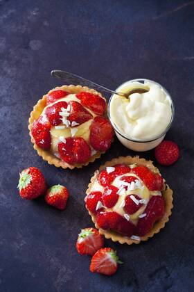 Two strawberry tartlets with custard and white chocolate shaving on dark ground  CSF28581