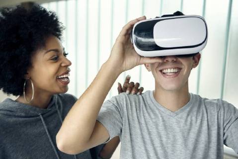 Young man using virtual reality simulator with friend  Copyright: DinocoxGreco B21478531