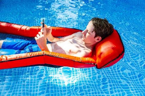 Boy floating on water in swimming pool using smartphone model released Symbolfoto  SARF03780
