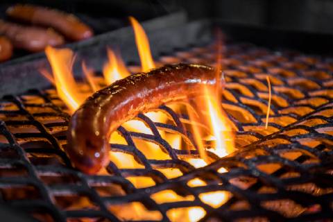 21.08.2018, Berlin, Deutschland, GER - Ein Würstchen liegt auf einem Rost und wird gegrillt.