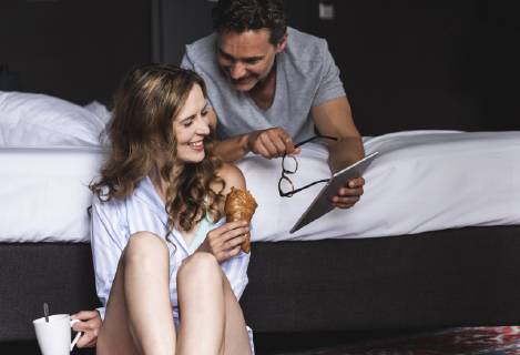 Happy couple in bedroom at home with tablet, coffee and croissant model released Symbolfoto UUF14388