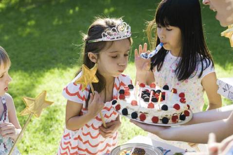 Girl blowing out candles on birthday cake at outdoor birthday party  Copyright: SigridxOlsson B58698206