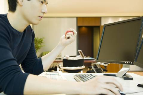 Office worker using computer, squeezing stress ball with one hand  Copyright: EricxAudras B39601717