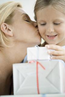 Mother kissing young daughter s cheek as girl looks at wrapped gifts  Copyright: LaurencexMouton B11138728