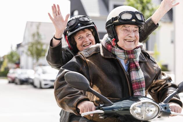 Happy senior couple having fun, riding motor scooter and waving model released Symbolfoto  UUF14920