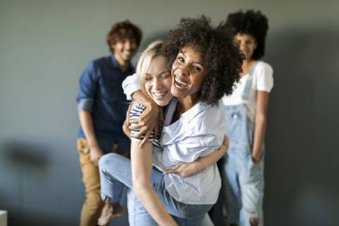 Two happy women hugging with friends in background model released Symbolfoto property released VABF01748