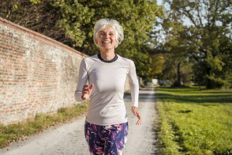 Happy senior woman running along brick wall in a park model released Symbolfoto DIGF05436