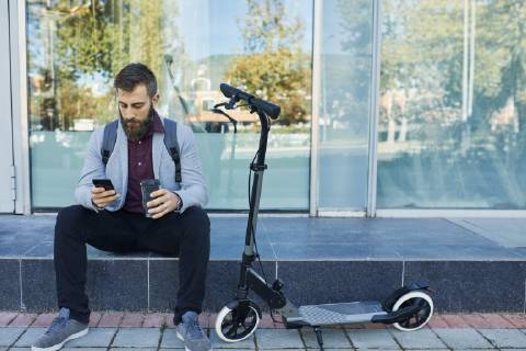 Businessman sitting outdoors using cell phone next to scooter model released Symbolfoto  ZEDF01702