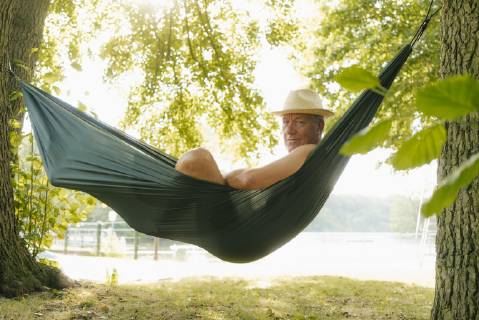 Senior man wearing straw hat relaxing in hammock at lakeshore model released Symbolfoto property released GUSF01783