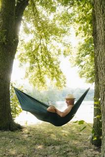 Senior man wearing straw hat relaxing in hammock at lakeshore reading book model released Symbolfoto property released GUSF01789